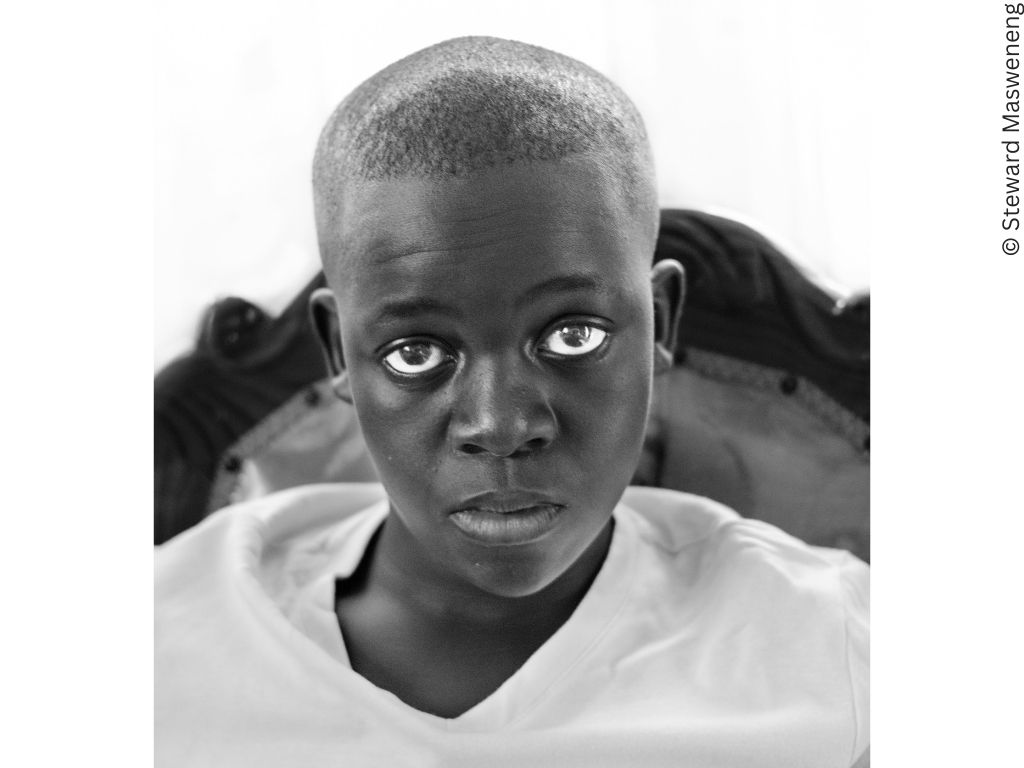 A young black boy looks at the camera with an inscrutable expression that might be weariness.