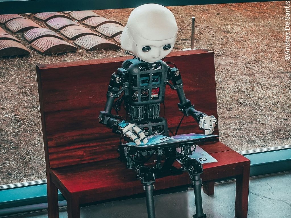 A robot child sits on a bench reading.