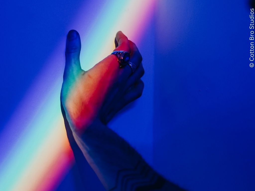 A hand rest against a wall. Rainbow-coloured light falls across it.