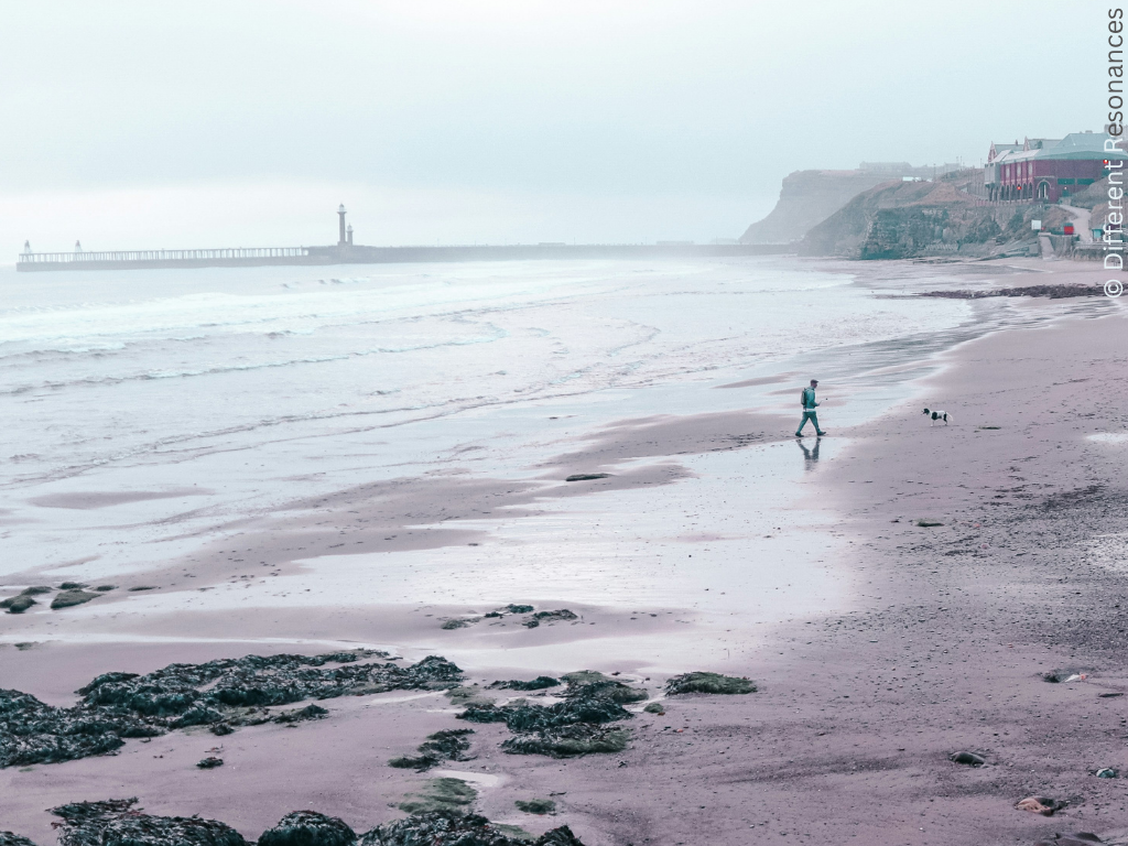 A northern shoreline in the UK. A person in the distance walks across the sand.