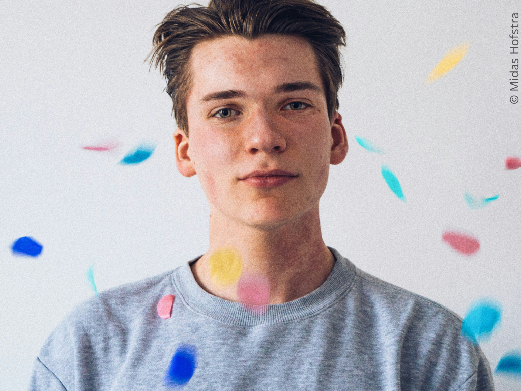 A young white man looks directly at the camera while colourful confetti falls.