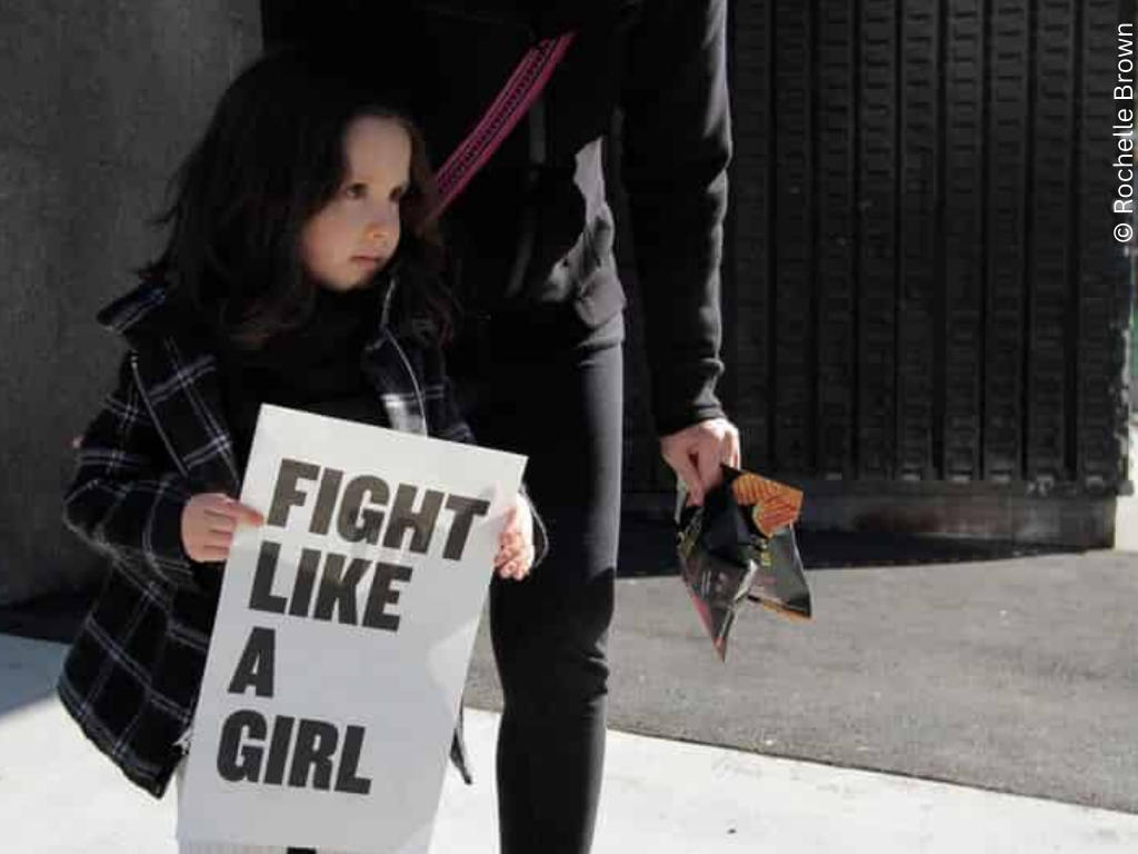 A girl holds a sign saying 'fight like a girl'