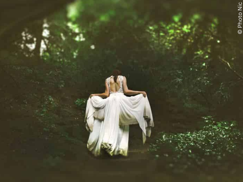 a woman in a white dress in the woods walking away