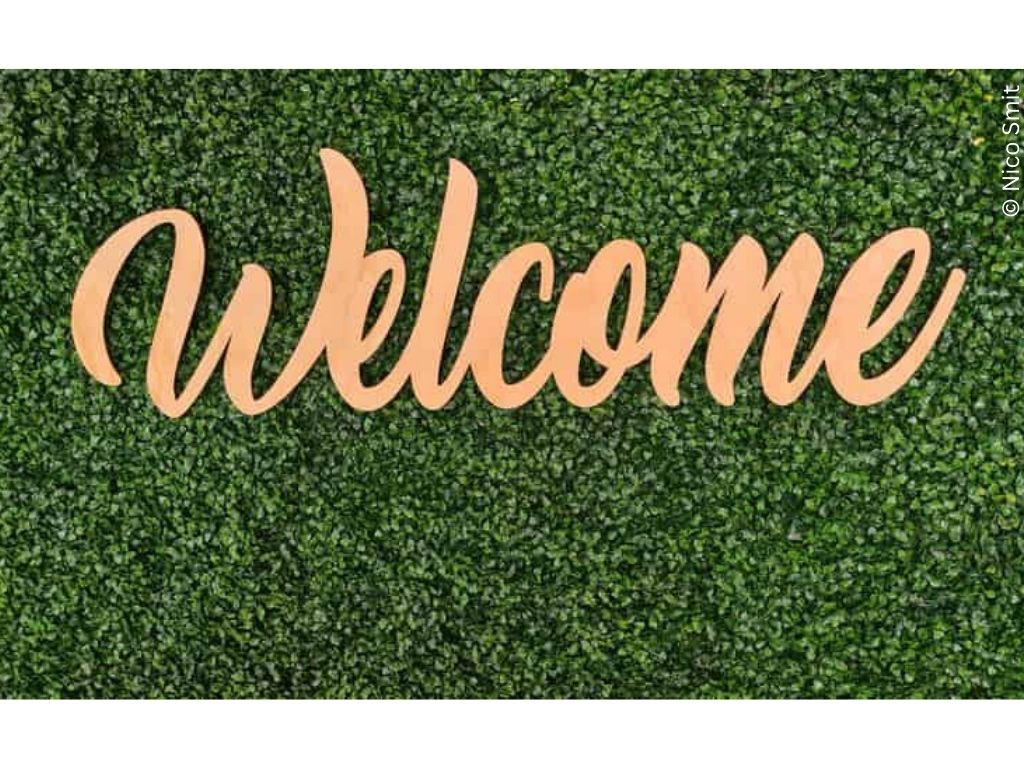 A golden 'welcome' sign laid across a leafy hedge